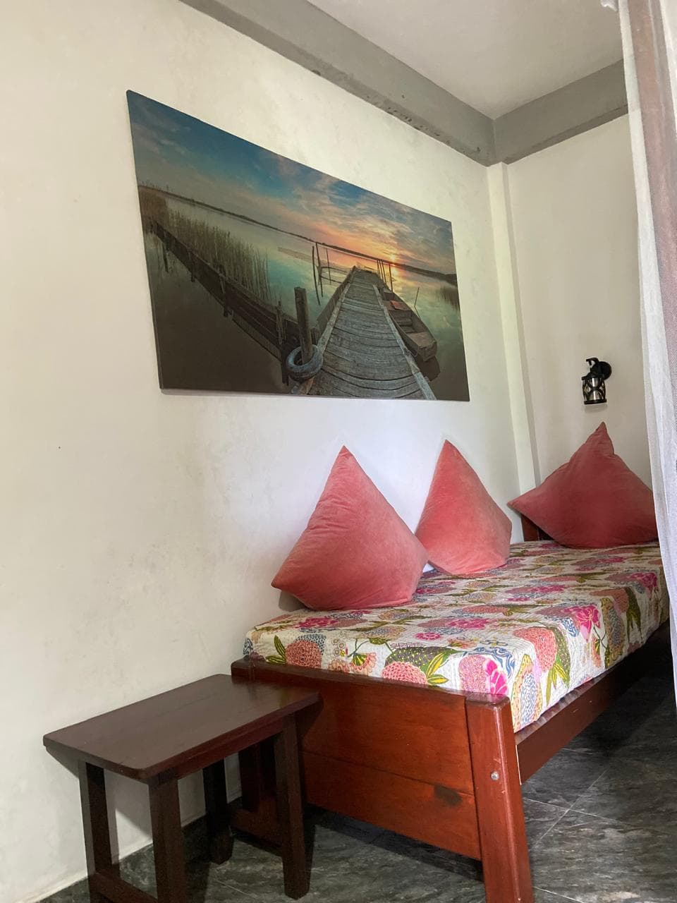 Single daybed with coral cushions beneath a jetty print