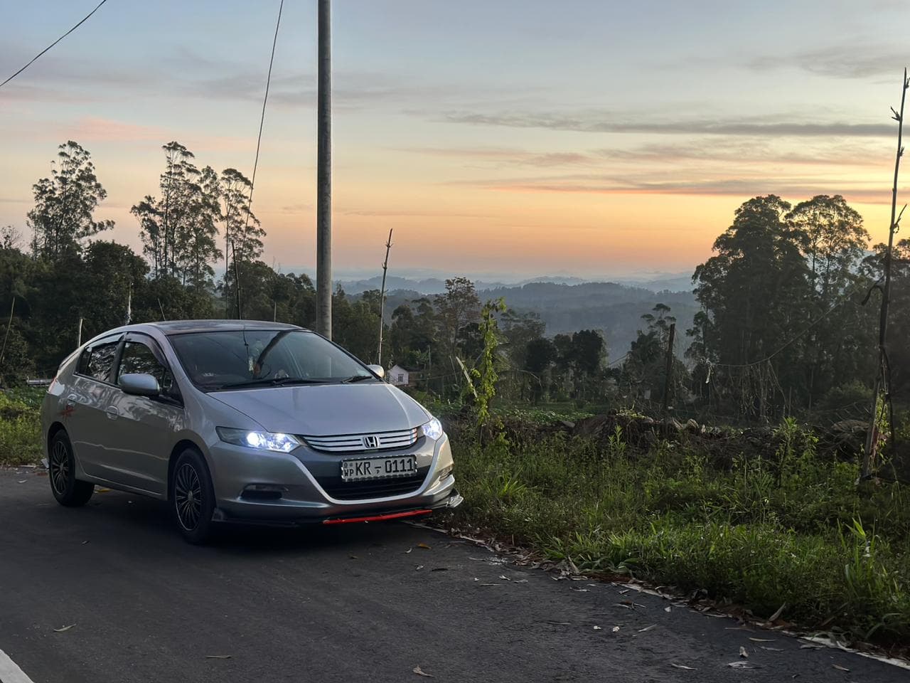 Silver sedan on a hillside road at sunset
